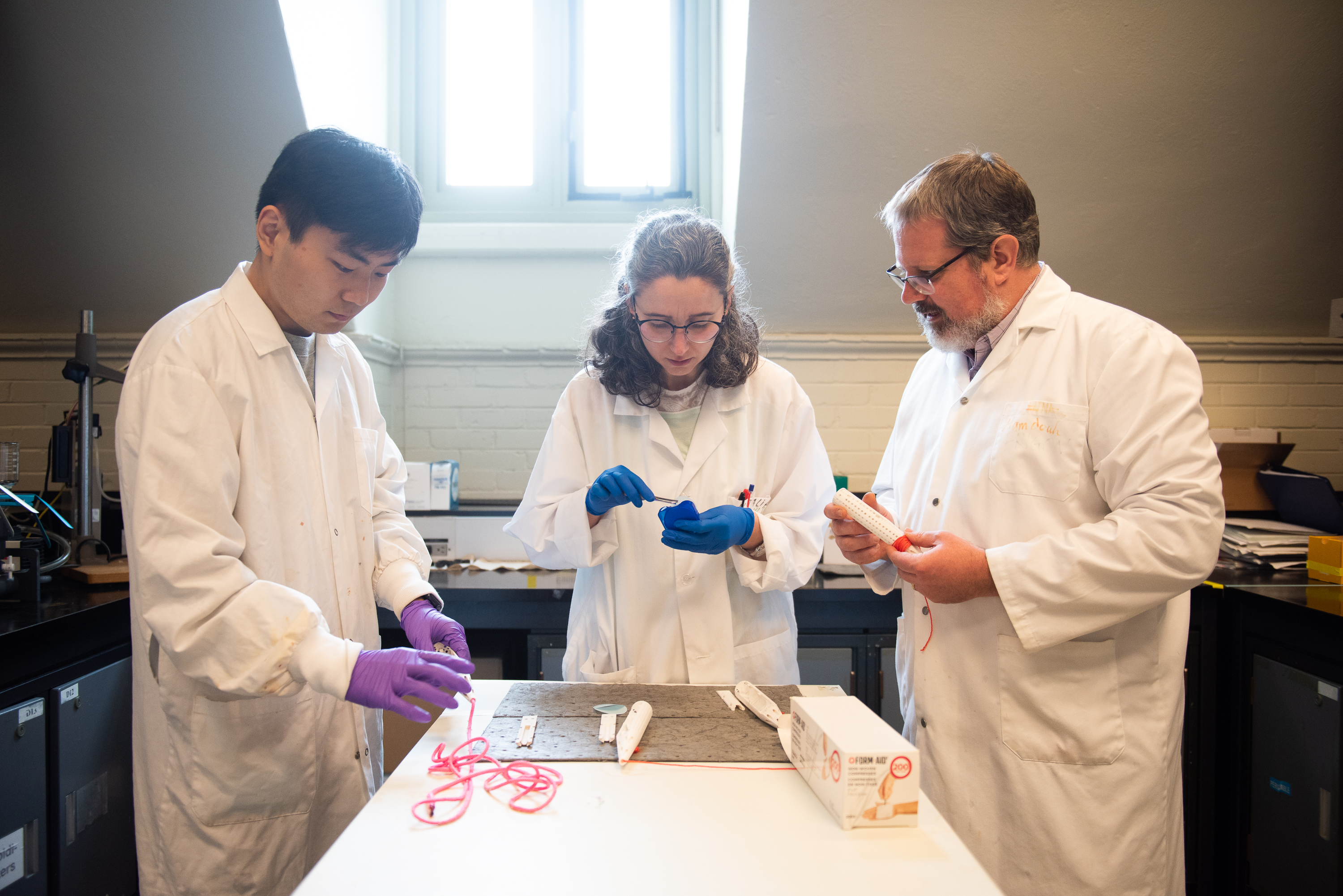 Two students in lab coats working in a lab alongside a teacher