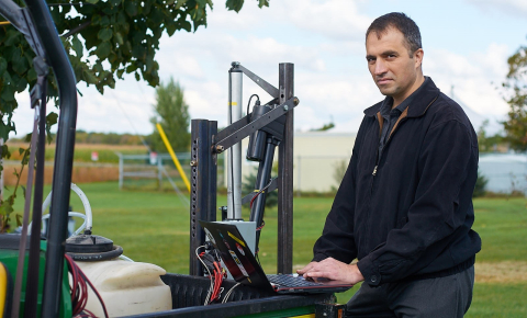 Dr. Viacheslav Adamchuk works at his laptop balanced on a tractor in the field