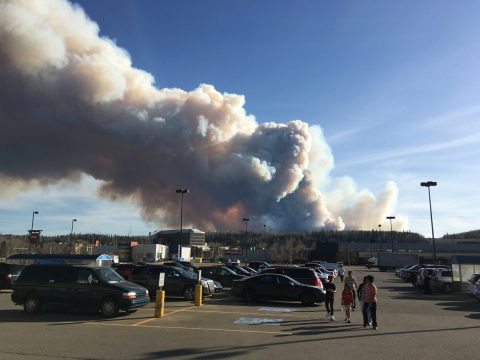 People look at clouds of wildfire smoke in the background from a parking lot in Fort MacMurray