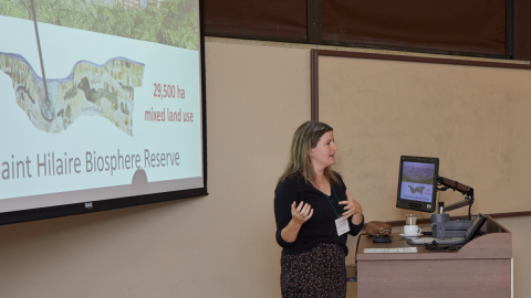 Jackie Hamilton presents her research to an audience, standing in front of a slide about the Saint Hilaire Biosphere Reserve