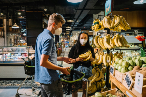 A man and a woman in a grocery store look at bunches of bananas