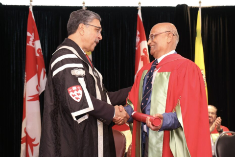 Vijaya Raghavan (right), dressed in regalia, shakes hands with Principal Deep Saini (left) as he receives McGill’s Lifetime Achievement Award for Leadership in Learning on stage during a convocation ceremony