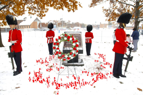 Uniformed mounties stand in formation around the war memorial at Macdonald Campus, adorned with a red and white wreath and mini Canadian flags planted in the snow.