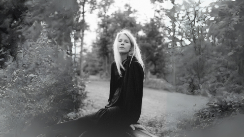 Shaina Hayes sits on a log outside with trees in the background, in black and white