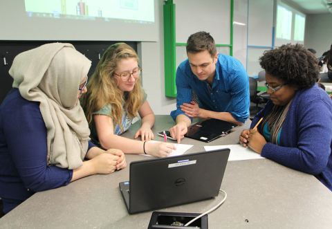 3 female students working at a table with their professor