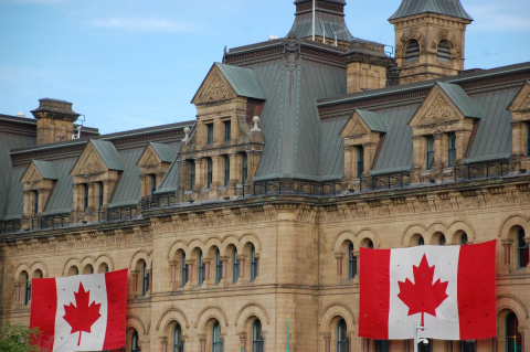 photo of Canadian Parliament building with a Canada flag in front 