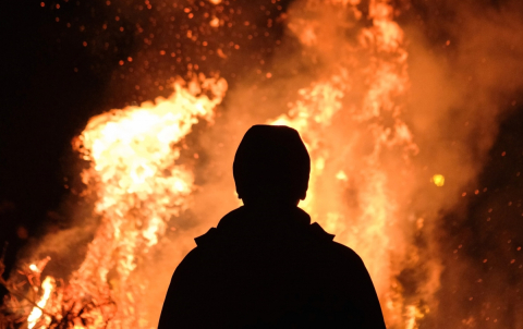 A man stands in front of a fire