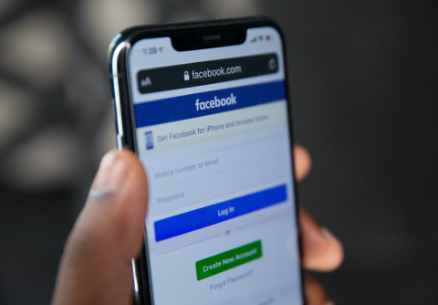 someone holding a phone with the Facebook login page clearly visible in the phone screen