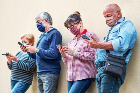 A line of people in masks look at content on their cell phones