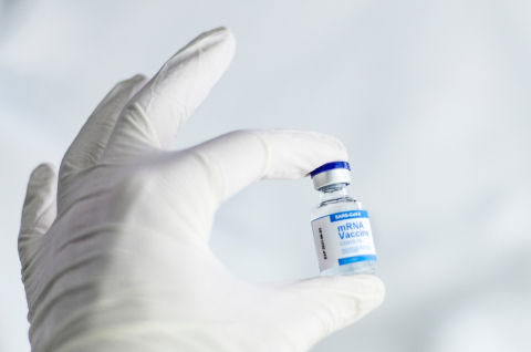 A person wearing a glove holds a vial of COVID-19 vaccine