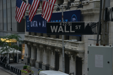 A street sign reads "Wall St." American flags drape the building behind the sign.
