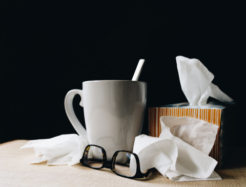 A mug of tea, a box of tissues, and a pair of glasses lay strewn out across a table