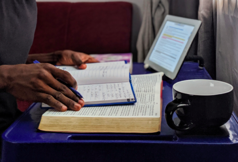 Hands taking notes while reading from book and tablet on a desk