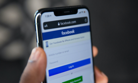 A person holds an iPhone with the Facebook login page open on its screen