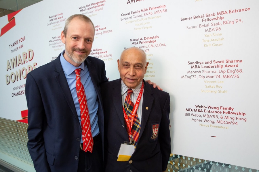 Alex King (Desautels Director of Development) and Mahesh Sharma (MEng’72, MBA’76) stand beside the sign posting the award donors and recipients.