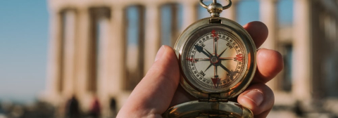 A hand holding a compass in front of the Acropolis