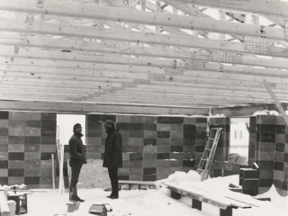 Two men stand in the Lessard House whilst it is being built