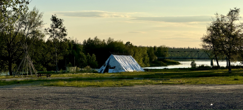 A traditional tent on a field of grass with a body of water in the background during the sunset.