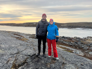Two Puvirnituq Doctors standing on a rock with the sunset over water in the background.