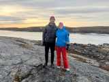 Deux Docteurs debout sur un rocher avec un coucher de soleil sur l'eau en arrière-plan.