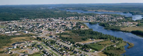 Vue aerienne d'un village avec une foret et de l'eau dans les alentours.