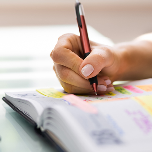 Hand holding pen, writing into a calendar