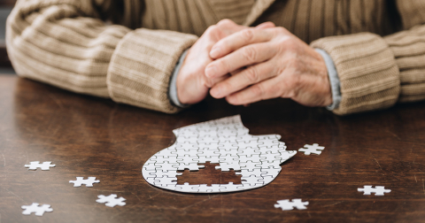 An elderly person completes a puzzle shaped like a human head 
