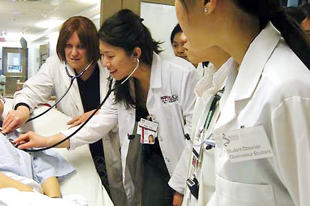 Several medical students leaning over a patient, listening with a stethoscope.
