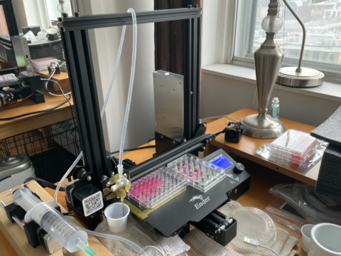 Collagen fabricator 3D printer on desk with white mug in bottom right corner