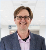 Marcel Behr wearing a grey suit, smiling