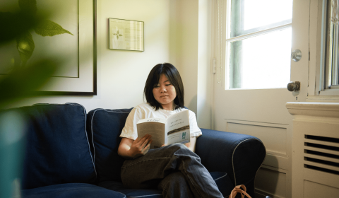 A student sits on a couch reading a book in the MORSL lounge.