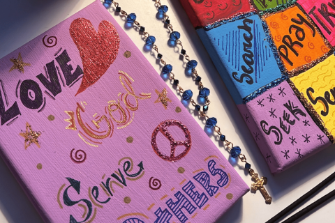 Closeup of Andrea's art project, canvas with painted letters reading "Love God Serve Others"