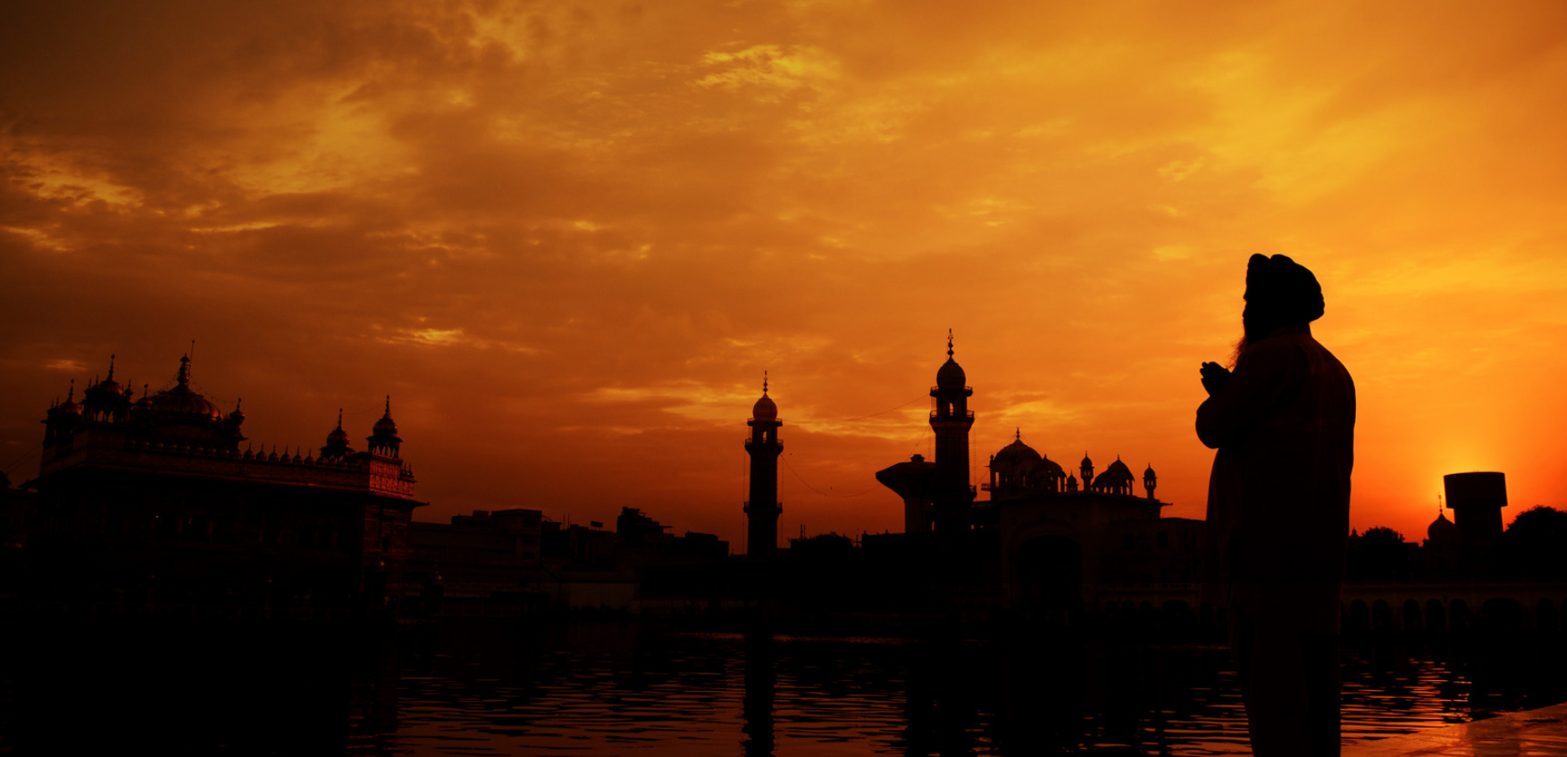 A Sikh man prays in front of an orange sunset