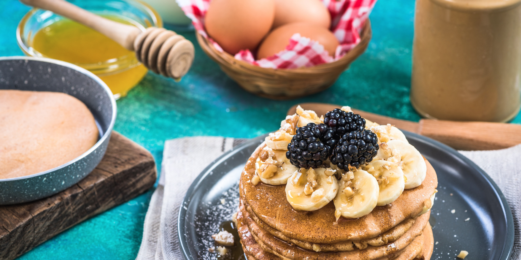 A stack of pancakes on a plate, surrounded by various ingredients (eggs and honey)