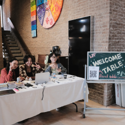 Three students sitting at welcome table at LPP conference smiling