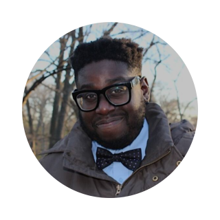 Emmanuel Tabi smiling outdoors in blue shirt with bow and glasses