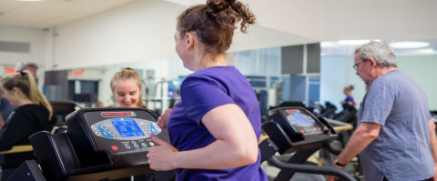 People exercising on treadmills in a gym with mirrored walls.