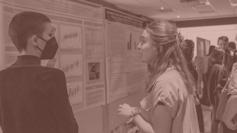 Student looking at a research poster while another student presents.