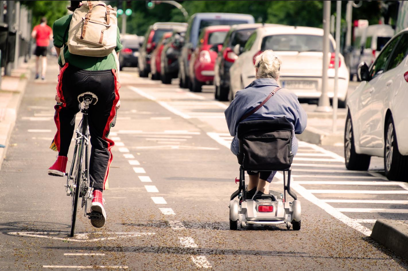 A cyclist and an elderly woman using a motorized scooter share a city bike path.