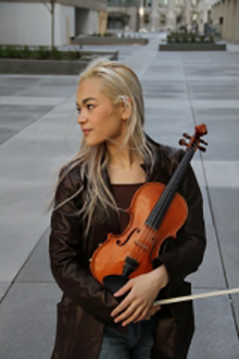 Astrid Nakamura holds violin in arms with bow in hand