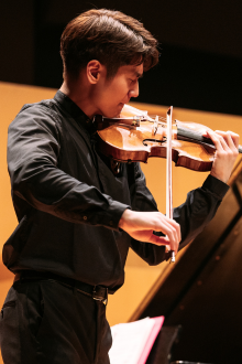 Man focused on music score while playing violin