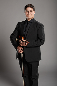 Frédérick Pouliot stands while smiling and holding violin and bow