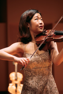 Asian woman playing violin with Golden Violin in background