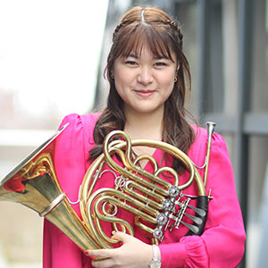 Woman holding french horn smiles at camera