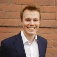 Headshot of a smiling Luke Reidlinger standing against a brick wall