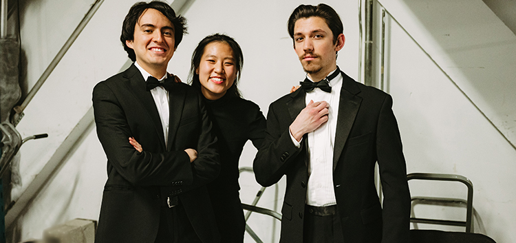 Two men dressed in black and white tuxedos and a woman in a black dress prepare for a performance 