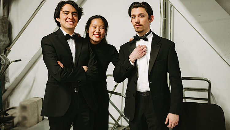 Three people dressed in black evening attire stand in various poses