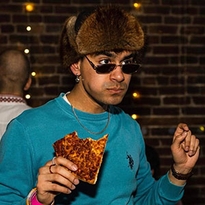 Man wearing hat and peering over sunglasses while holding a bitten slice of toast