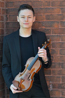 Photo of Russell Iceberg leaning against  brick wall while holding a violin