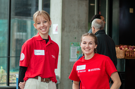 Two smiling female students wearing Schulich School of Music red t-shirts are ready to welcome visitors
